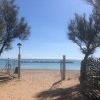 Ingresso di una spiaggia sabbiosa con due alberi e un lampione. Il mare è calmo in lontananza.