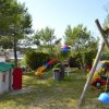 Parco giochi con altalene, scivoli, una casetta in miniatura e un'automobile giocattolo colorata.